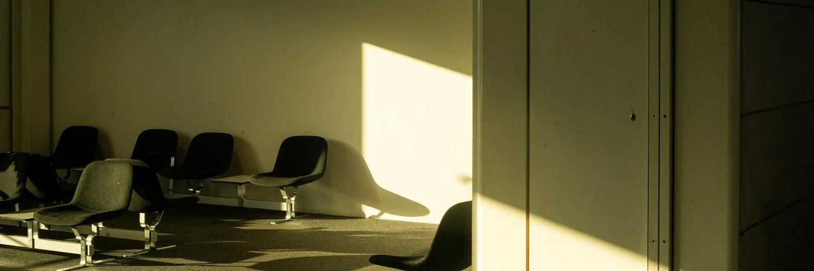 An empty institutional waiting area with rows of bench seats and raking sunlight
