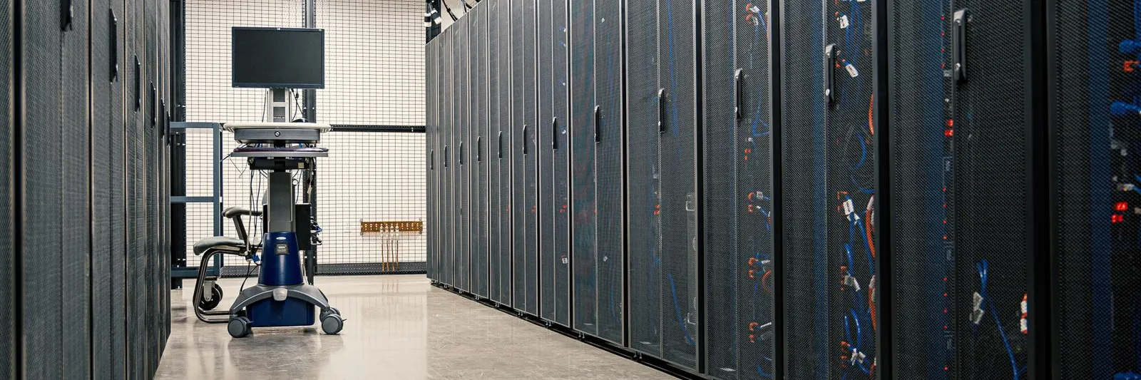 A corridor of black server racks with blue patch cables in a clean data centre