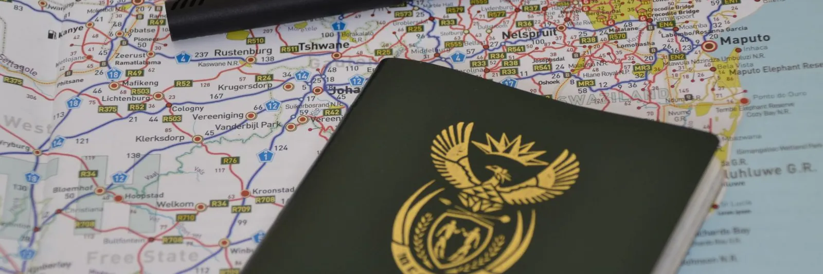 A closed Republic of South Africa passport (green cover, coat of arms, English/French/Afrikaans titles) lying on a detailed road map of South Africa, with a bla